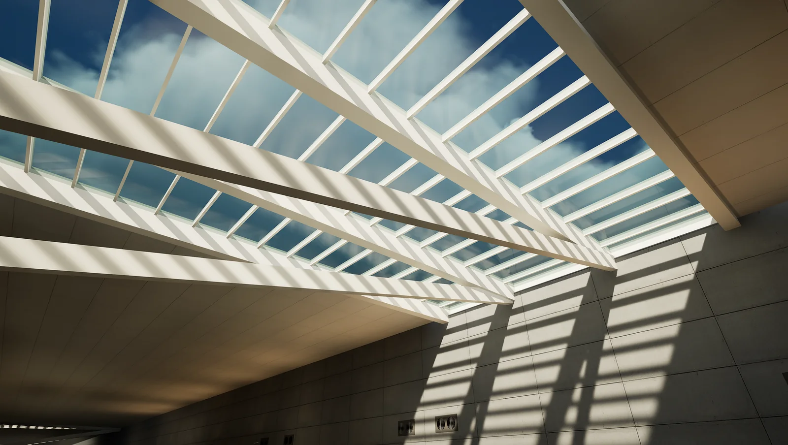Daylight falling through a clerestory roof structure into the ticketing hall, casting angled shadows down the wall